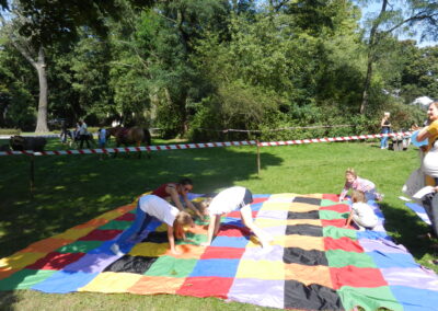 Warsztaty ruchowe, grupka gimnastykujących się dzieci na patchworkowej macie na trawie